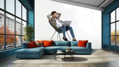 Young smiling businessman sitting in office chair and working on laptop on white background Wall mural